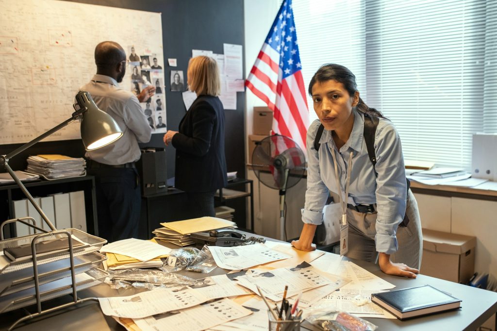 Young serious Hispanic female detective bending over workplace with documents